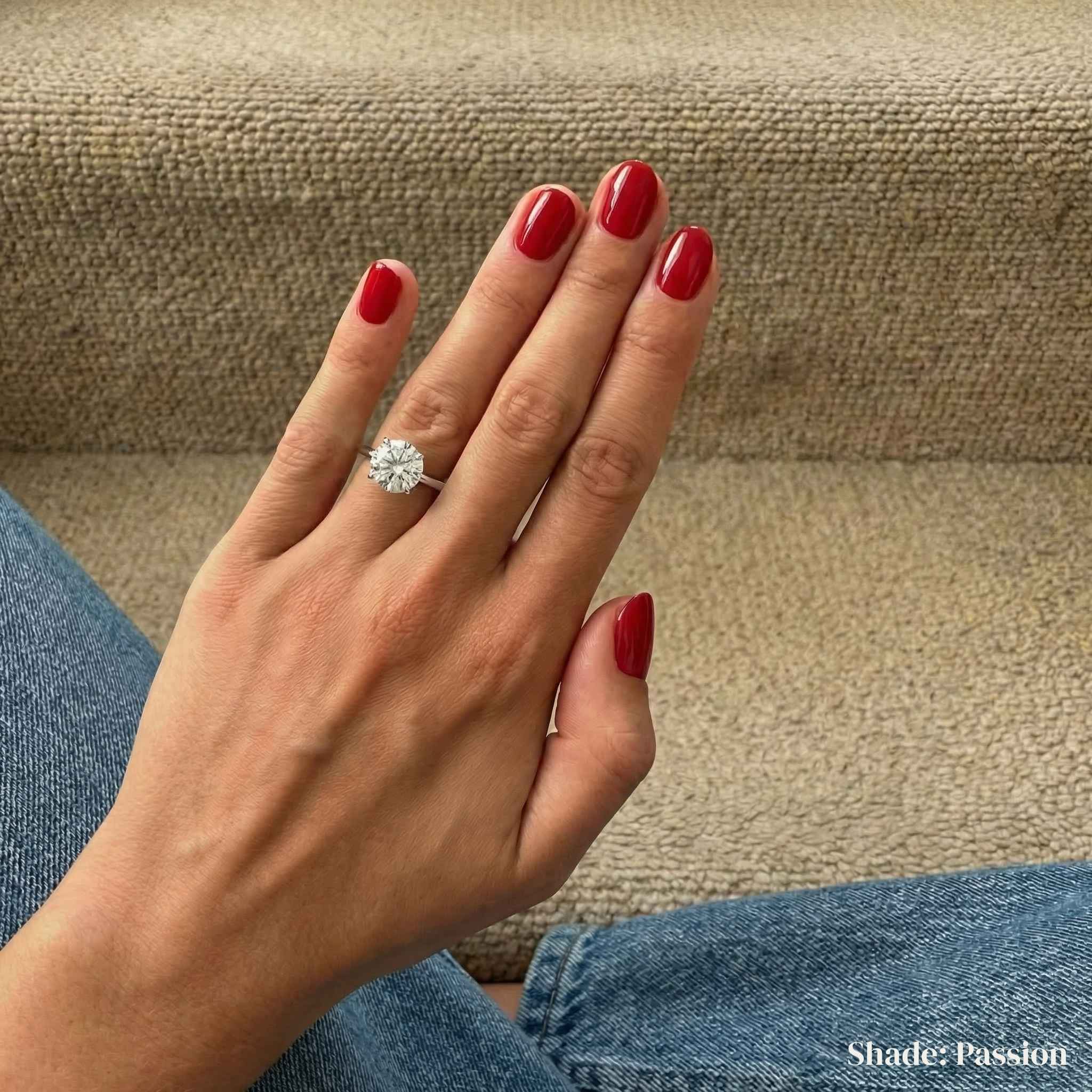 Hand with red nail polish wearing a diamond ring on a beige surface