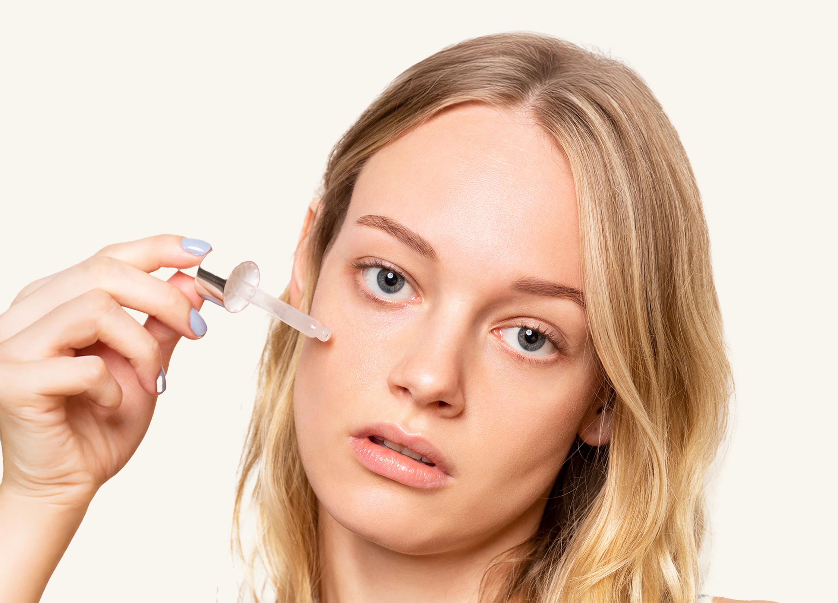Woman applying eye drops with a dropper on a plain background