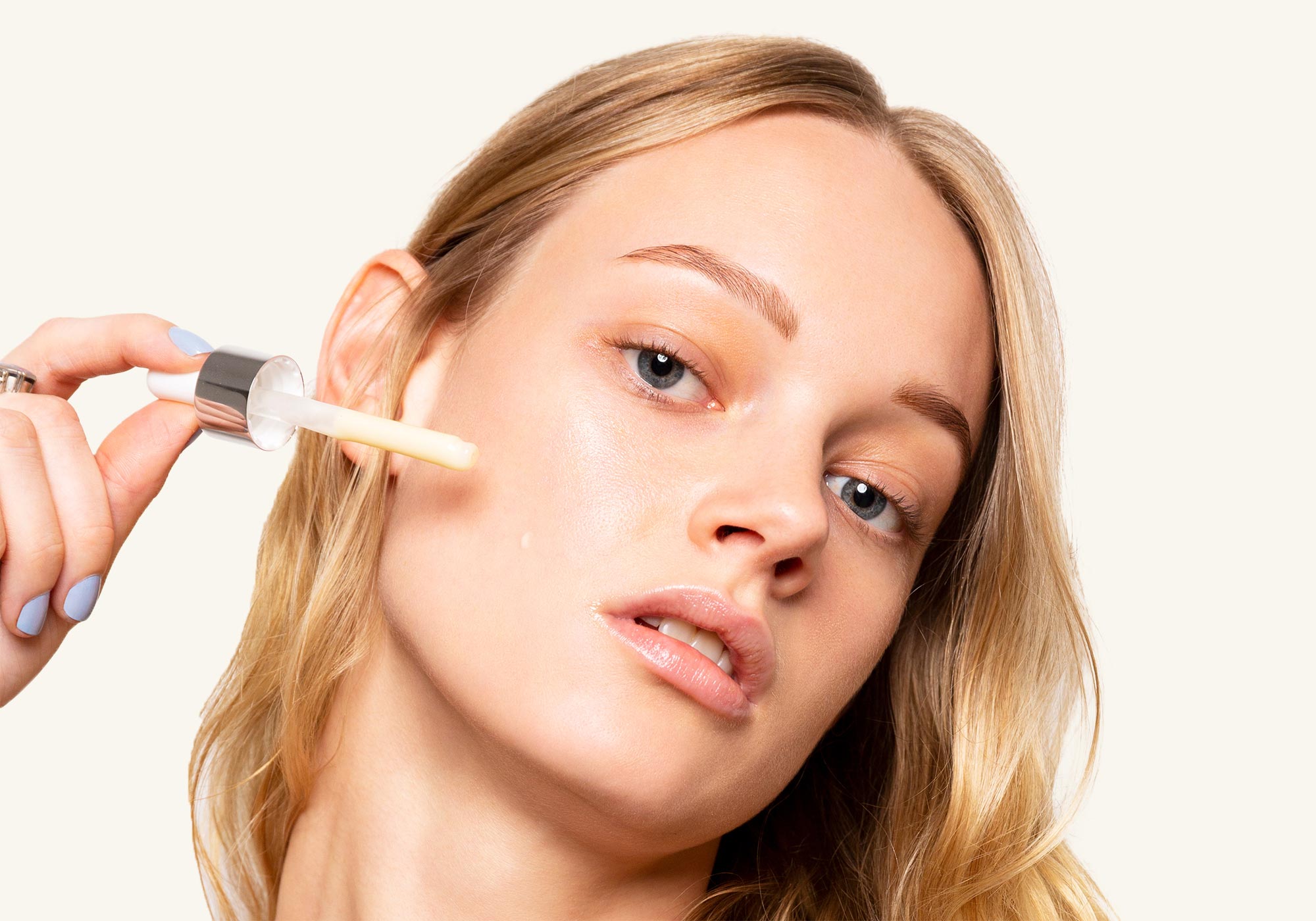 Model applying SCOUT Vitamin C Brightening Serum with dropper to cheek, showing dewy skin and effortless radiance.