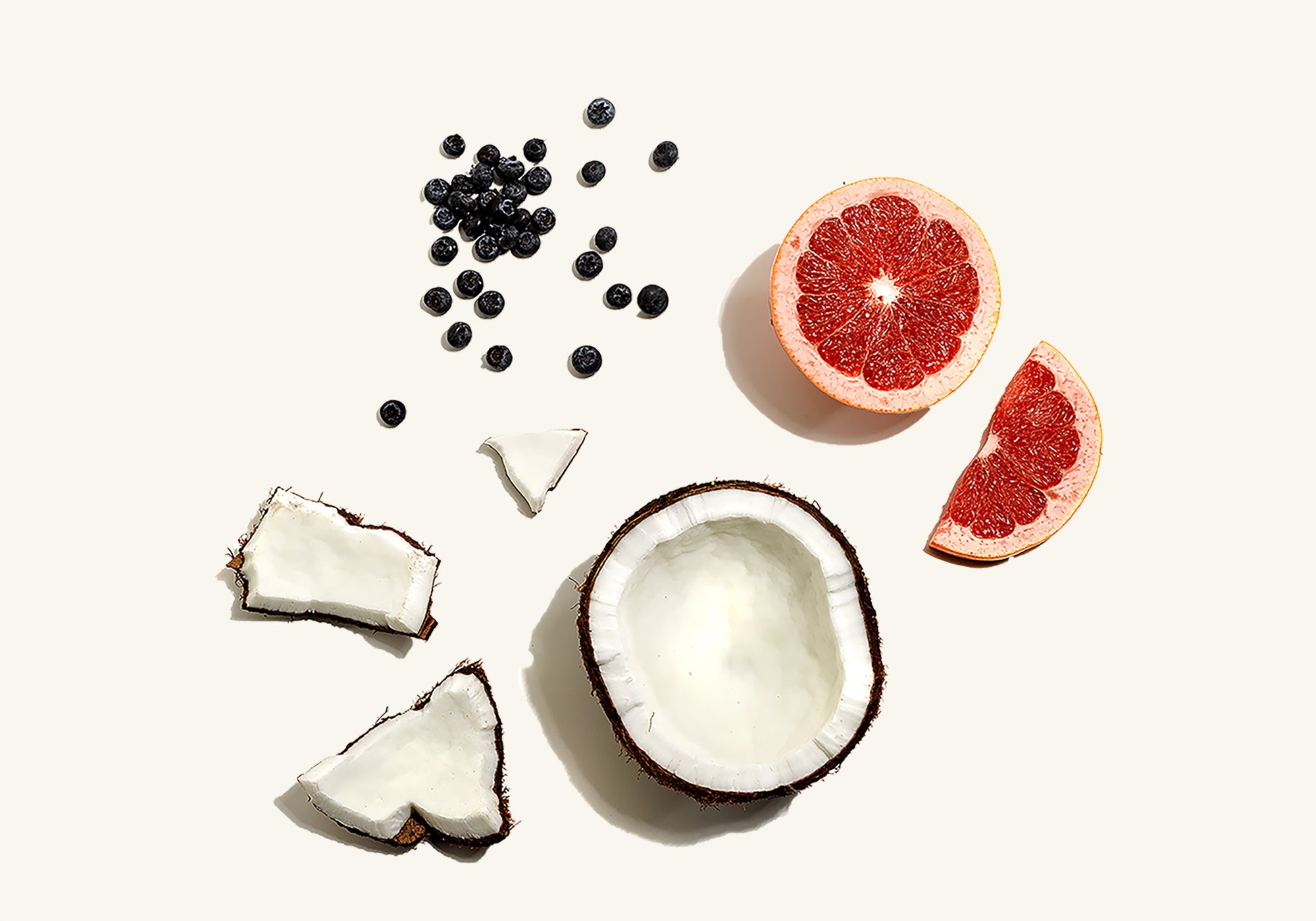Coconut halves, grapefruit, and blueberries arranged on a white background