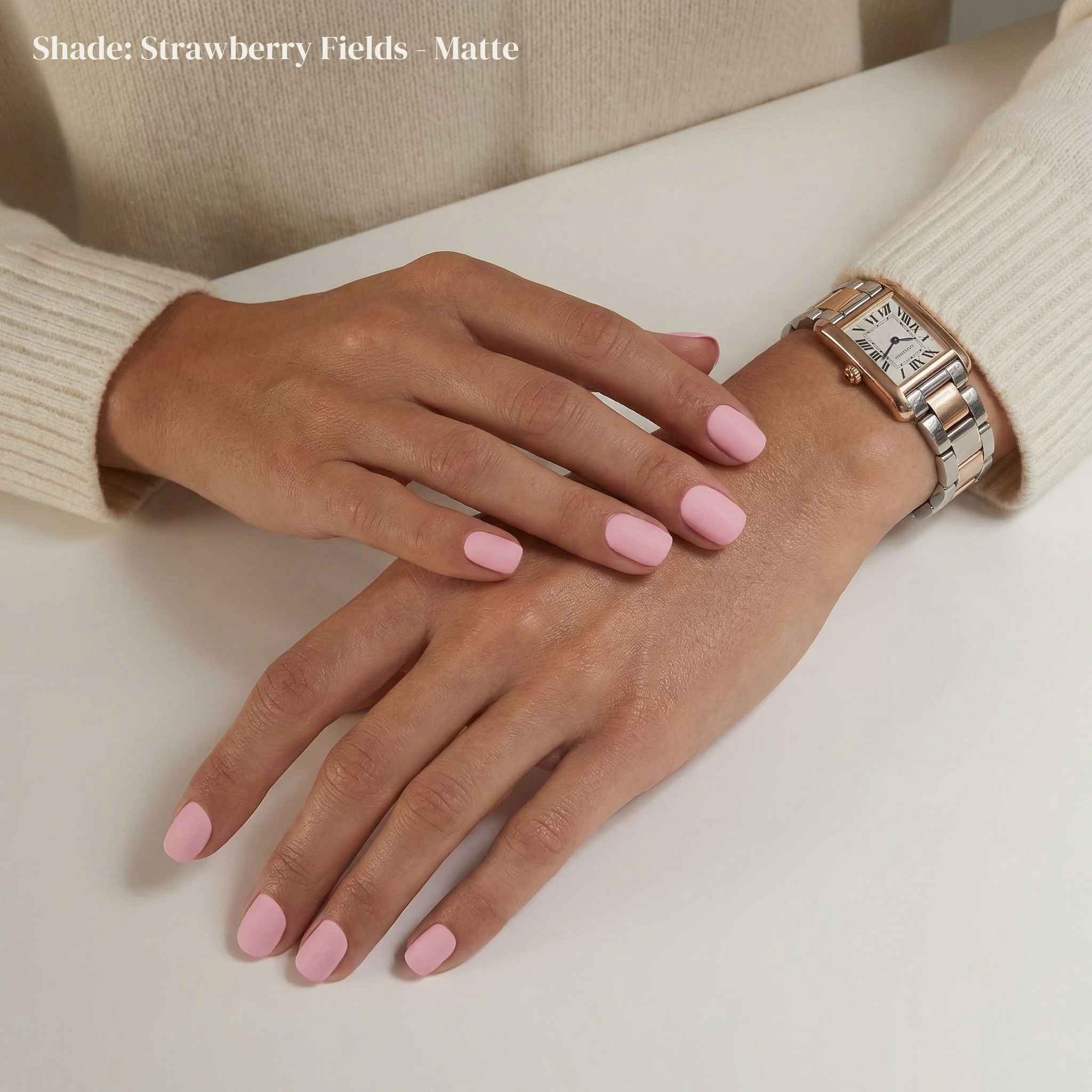 Hand with pink nail polish wearing a watch on a neutral background