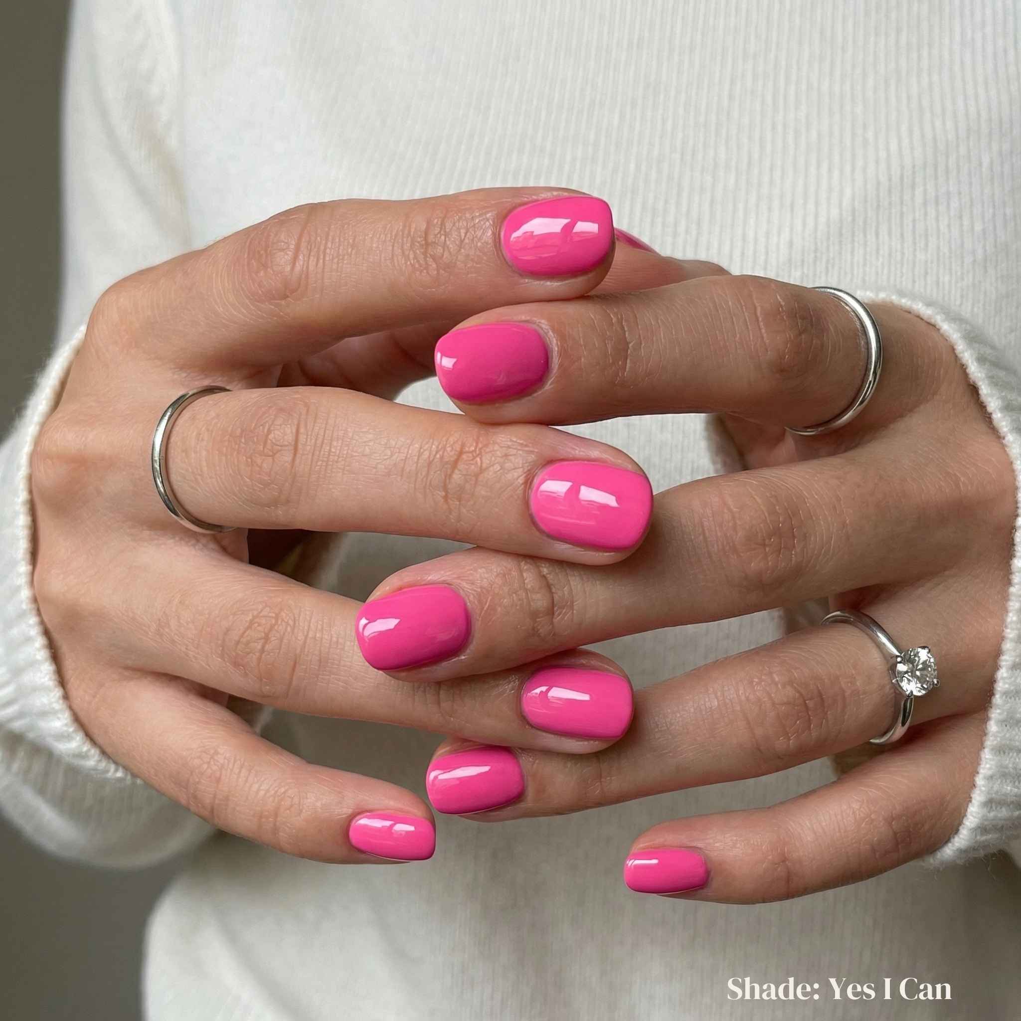 Close-up of hands with bright pink nail polish wearing silver rings on a neutral background