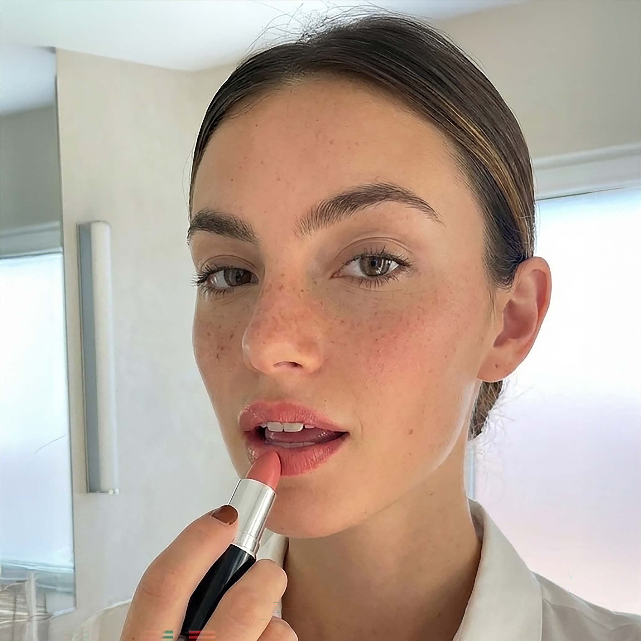 Woman applying lipstick indoors with a neutral background