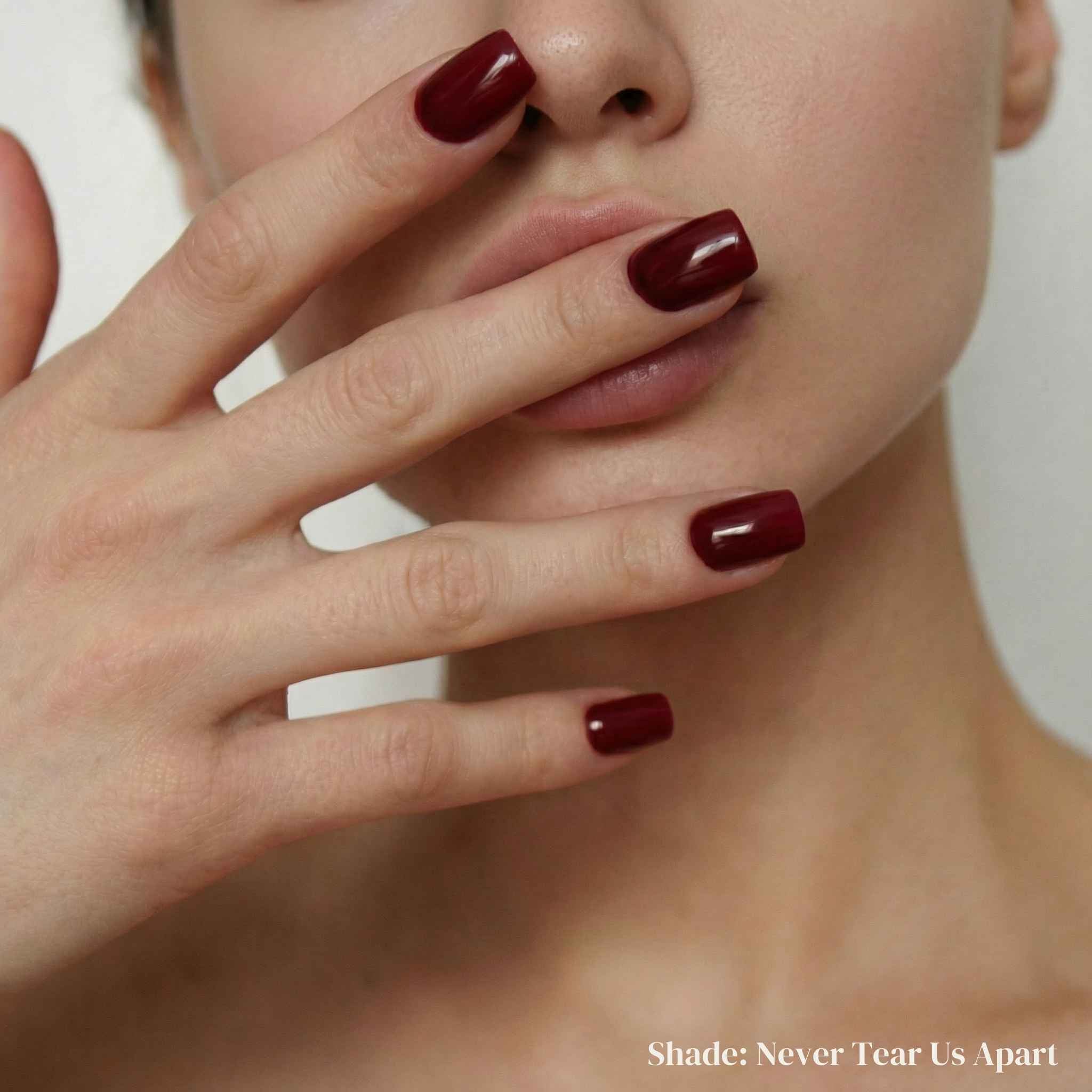 Close-up of a person's hand with dark red nail polish covering part of their face.
