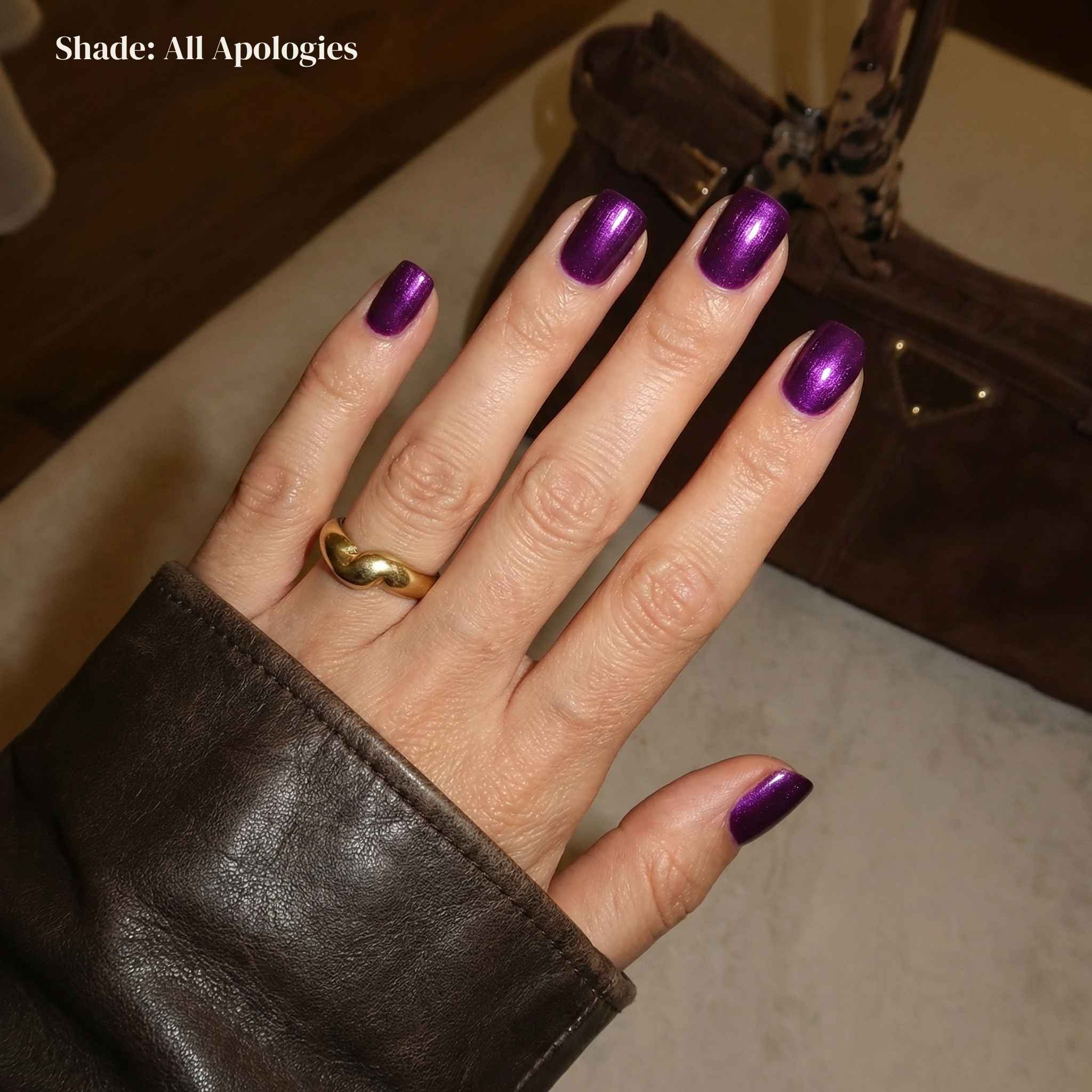 Hand with purple nail polish wearing a gold ring, with a blurred background.