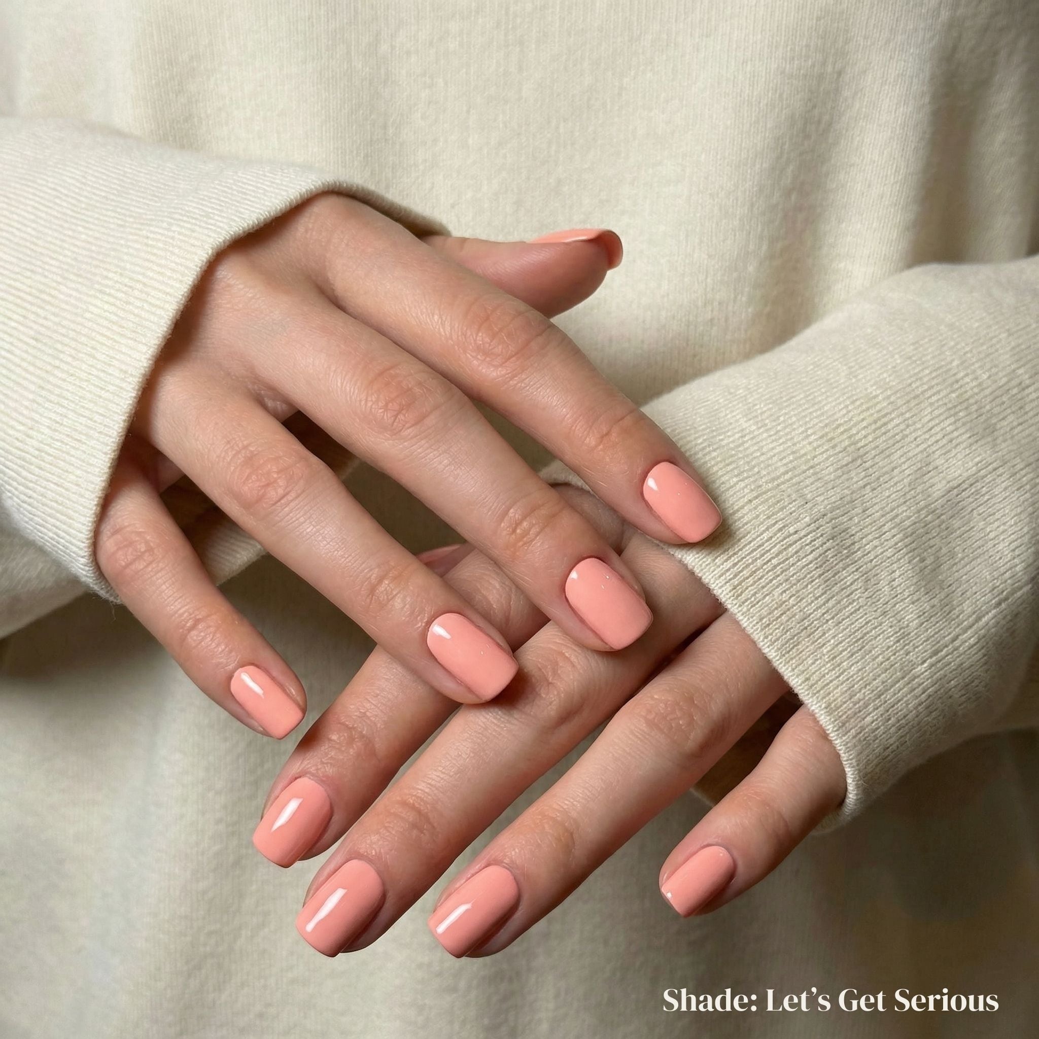 Close-up of hands with pink nail polish wearing a beige sweater.