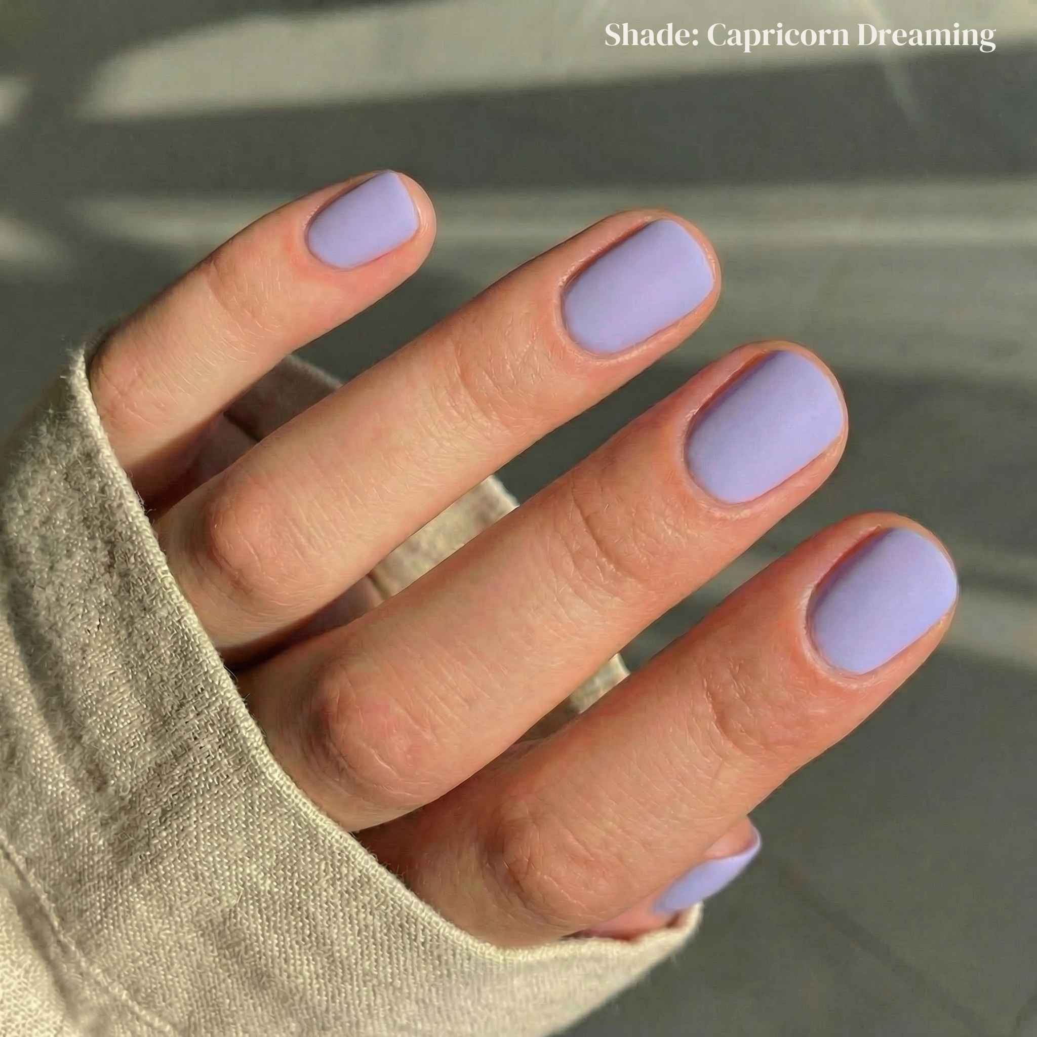 Hand with light purple nail polish on a neutral background