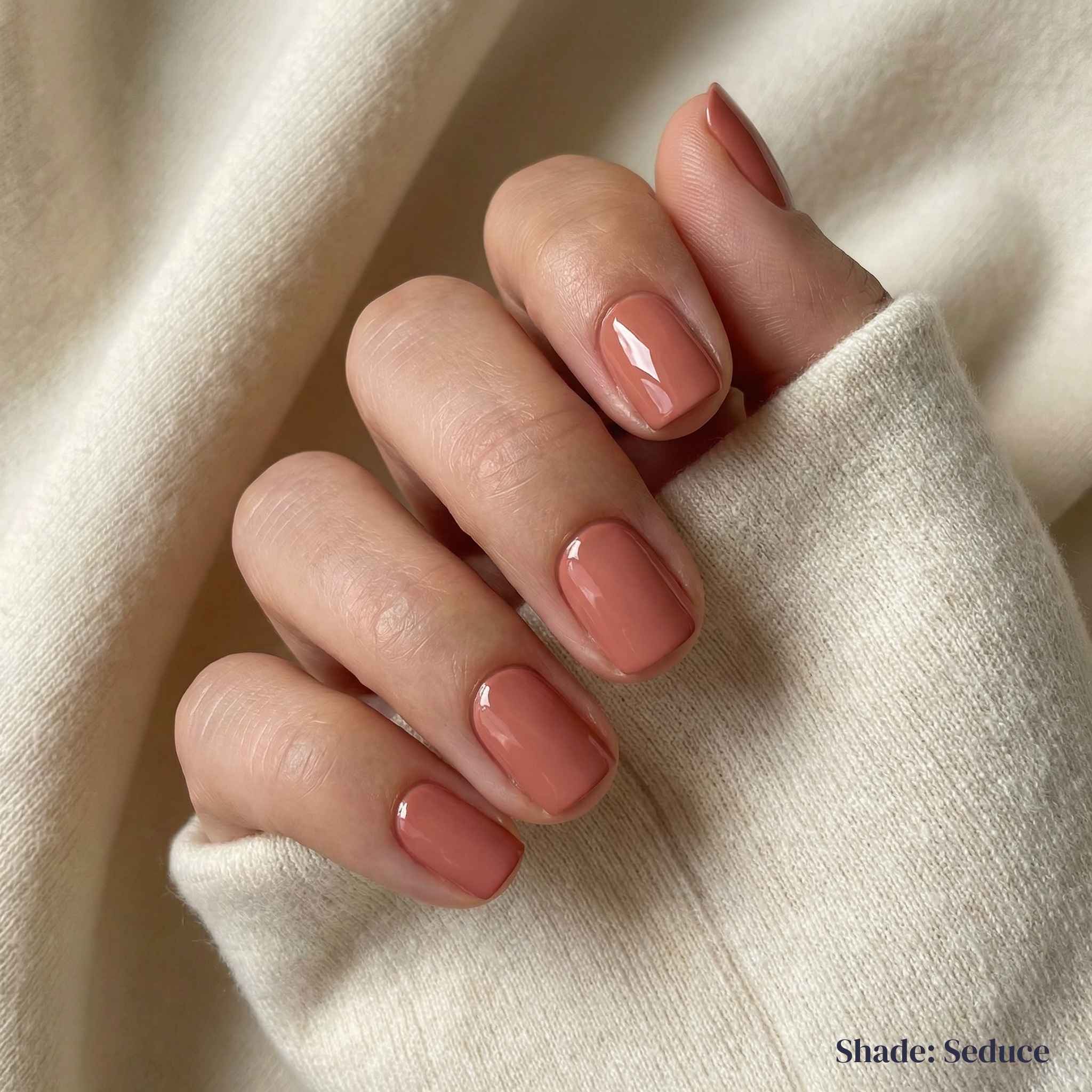 Hand with pink nail polish on a beige fabric background