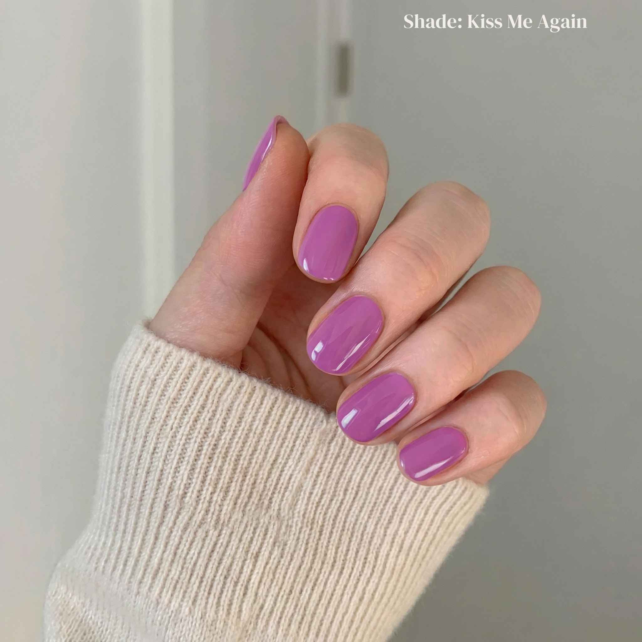 Hand with purple nail polish wearing a beige sleeve against a neutral background