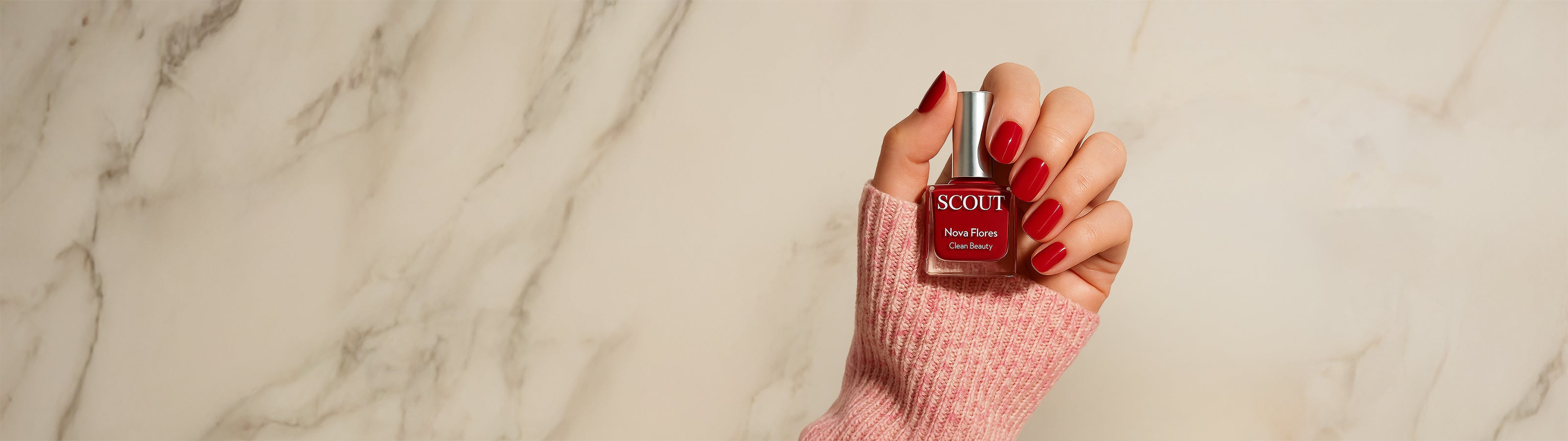 Hand holding a small bottle of nail polish with 'SCOUT' branding on a marble background