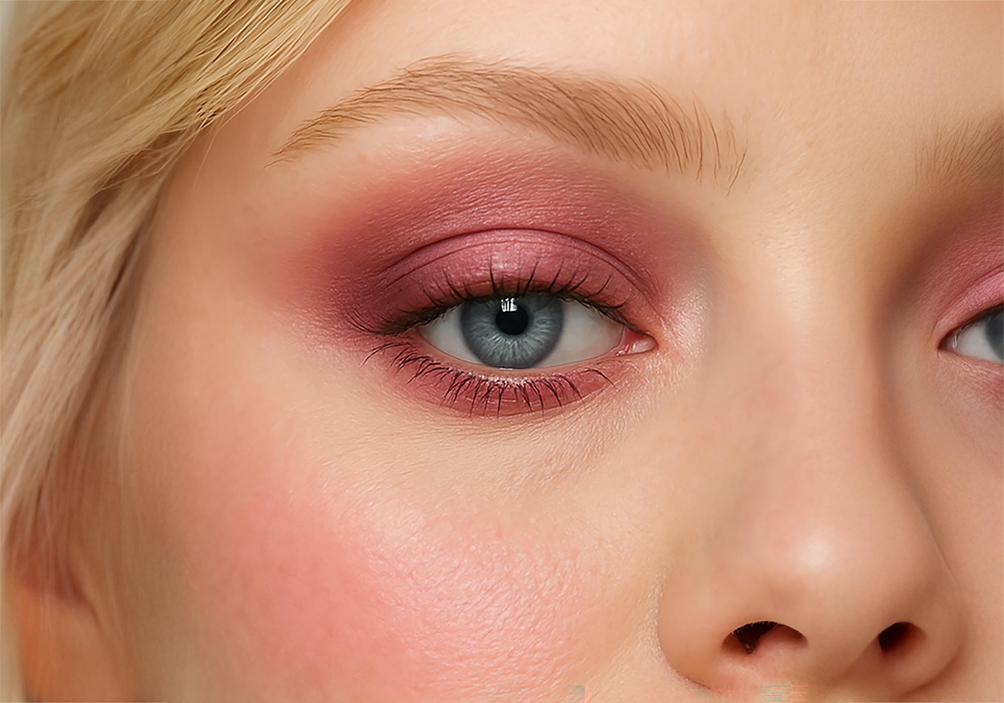 Close-up of a person's eye with pink eyeshadow and blonde hair.