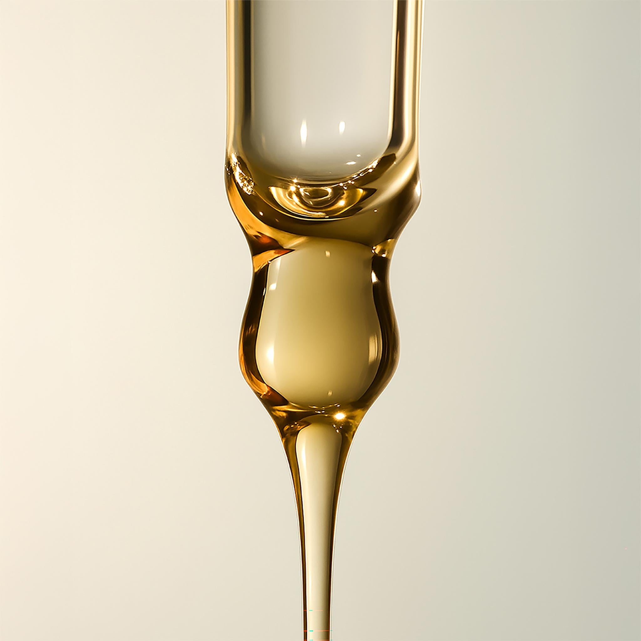 Close-up of a glass with a thin stream of liquid being poured against a neutral background
